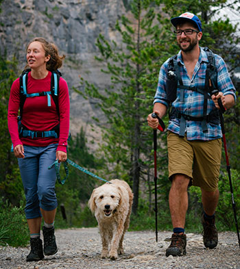 Deux randonneurs marchant avec un chien en laisse.