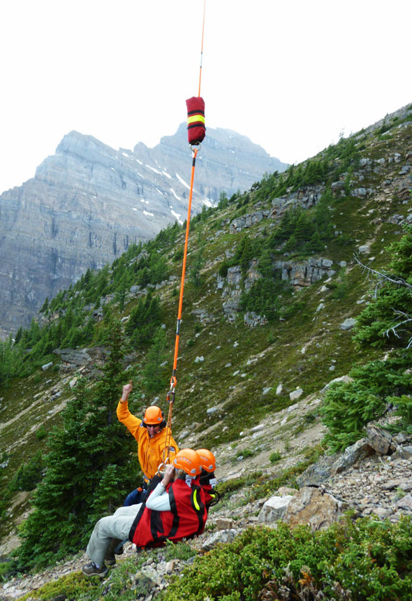 A Visitor Safety Specialist slinging the first subject from the ledge as the second specialist rigs the second subject. 
