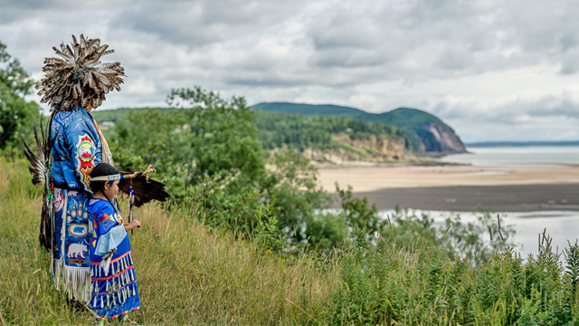 Silhouette d’une personne mi’kmaq en tenue traditionnelle, sur fond de ciel bleu.