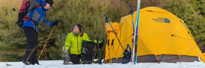 Un couple font du camping d'hiver. Leur tente est sur la neige.