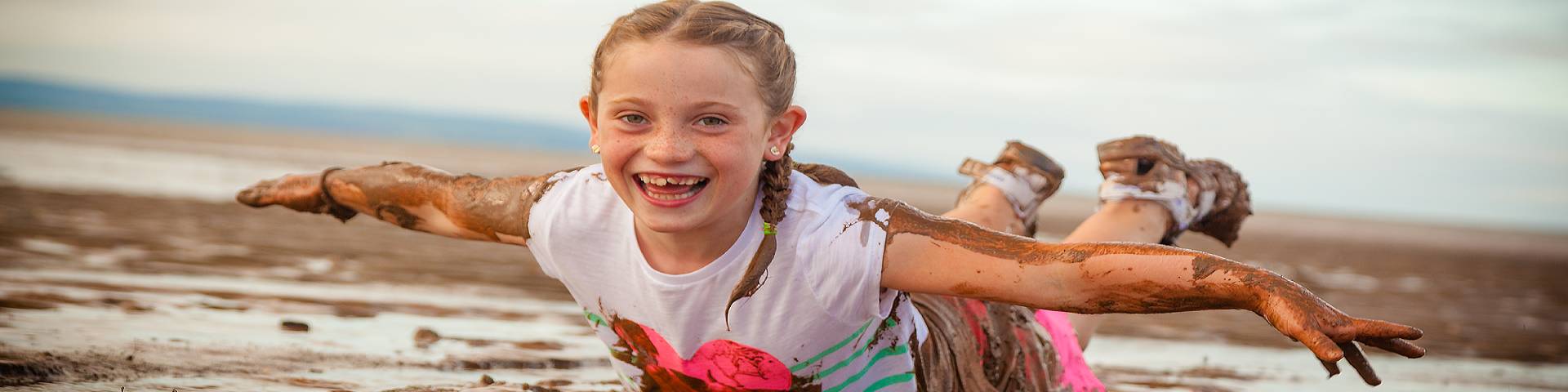 A girl sliding on her stomach in the muddy beach water