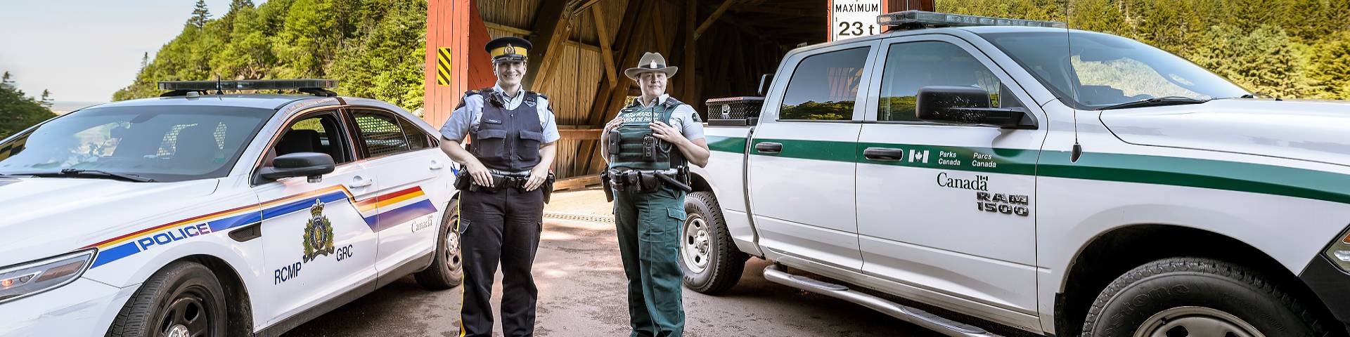 A park warden and an RCMP officer standing next to their vehicles