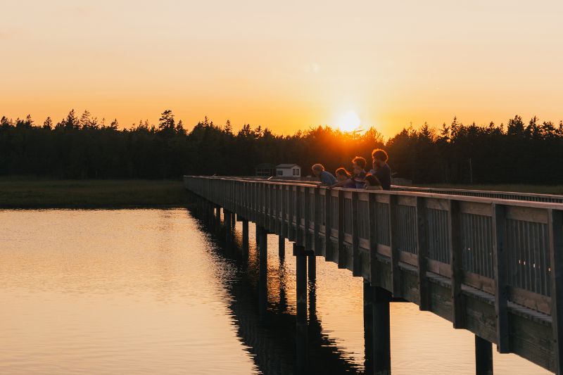 Une famille sur un pont piétonnier au-dessus d'un plan d'eau au coucher du soleil