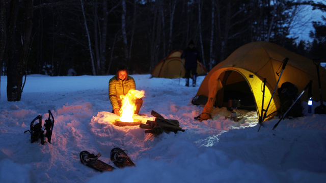 Une visiteuse est assise près du feu de camp, près de sa tente, en hiver.