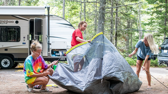 Three campers setting up their tent near their trailer.