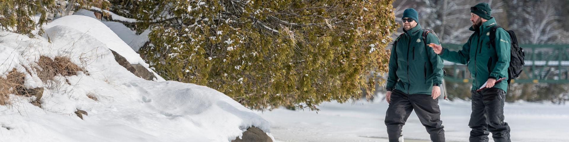 Resource conservation employees walk on a frozen river while monitoring river otter activity.