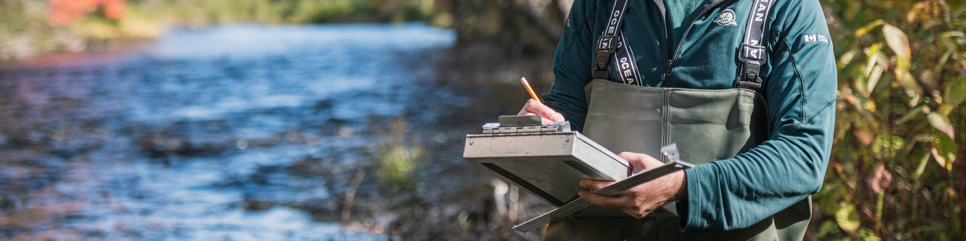 A Conservation officer stands next to a river, writing notes.