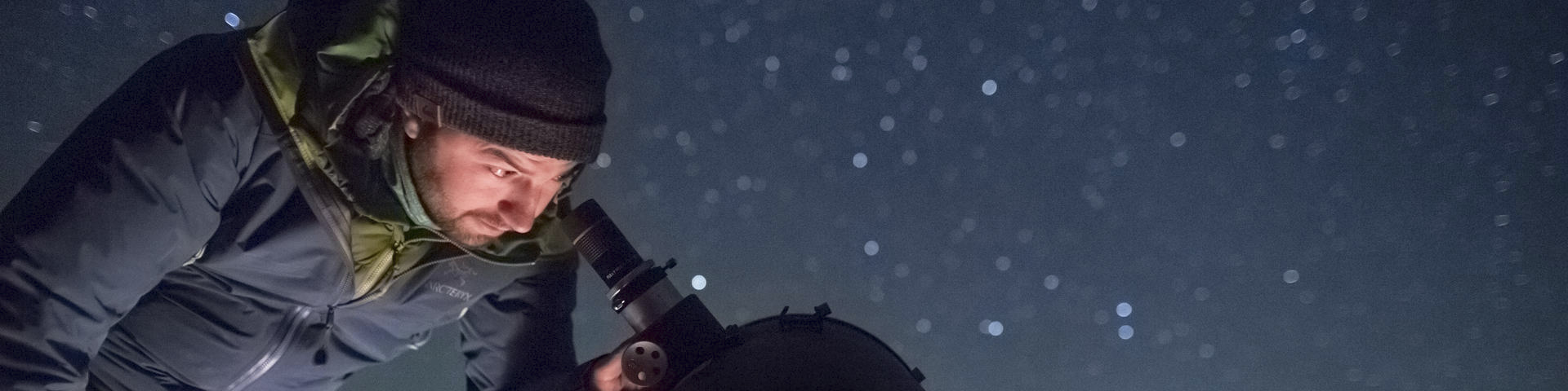 A man looks in a telescope at night