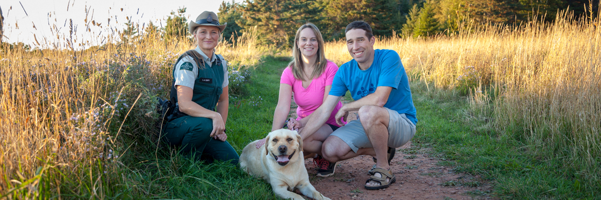 A park warden stops on a trail to talk to visitors with a dog