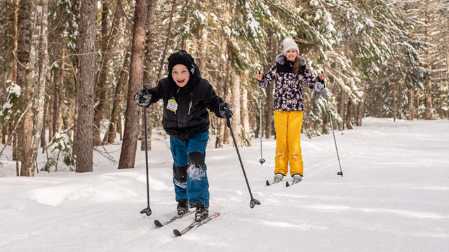 Deux visiteurs en train de faire du ski de fond sur une piste damée dans la forêt.