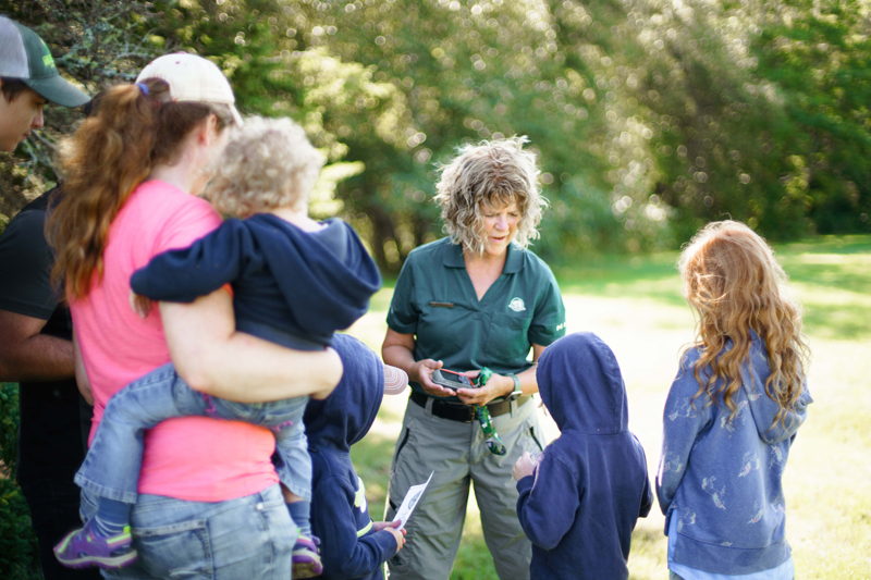 A Parks Canada interpreter speaking to a group of visitors holding a geocache.