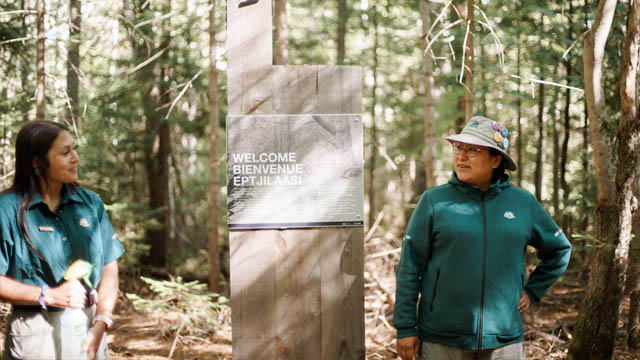 Two Parks Canada staff members in the forest, near an interpretation panel