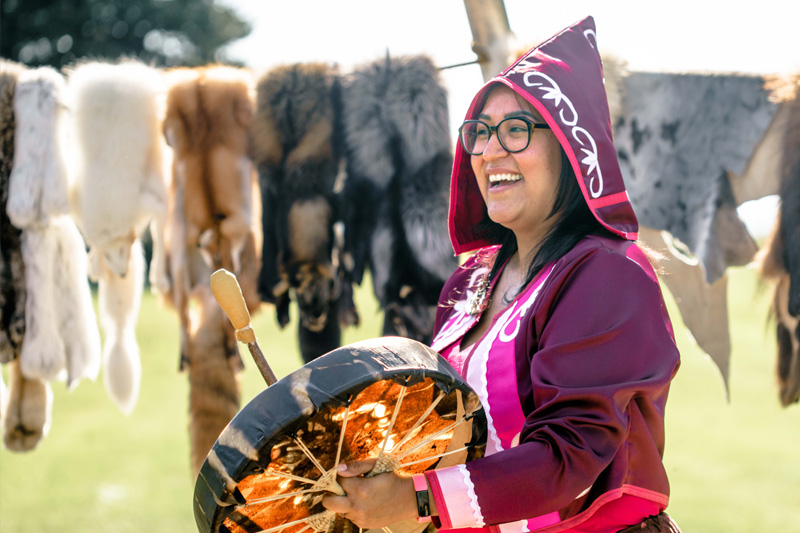 An interpreter dressed in traditional Indigenous clothing, drumming. 