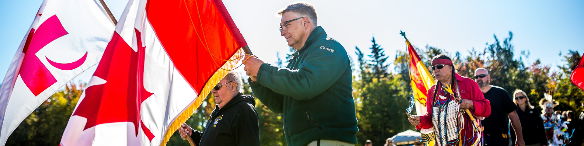 Des membres des peuples autochtones et des employés de Parcs Canada brandissant les drapeaux mi'kmaq et canadien lors d'une célébration.