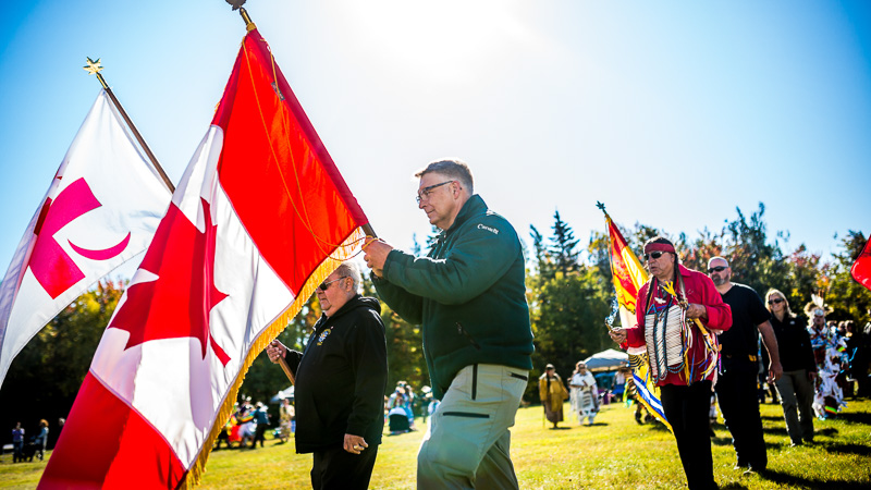 Des membres des peuples autochtones et des employés de Parcs Canada brandissant les drapeaux mi'kmaq et canadien lors d'une célébration.