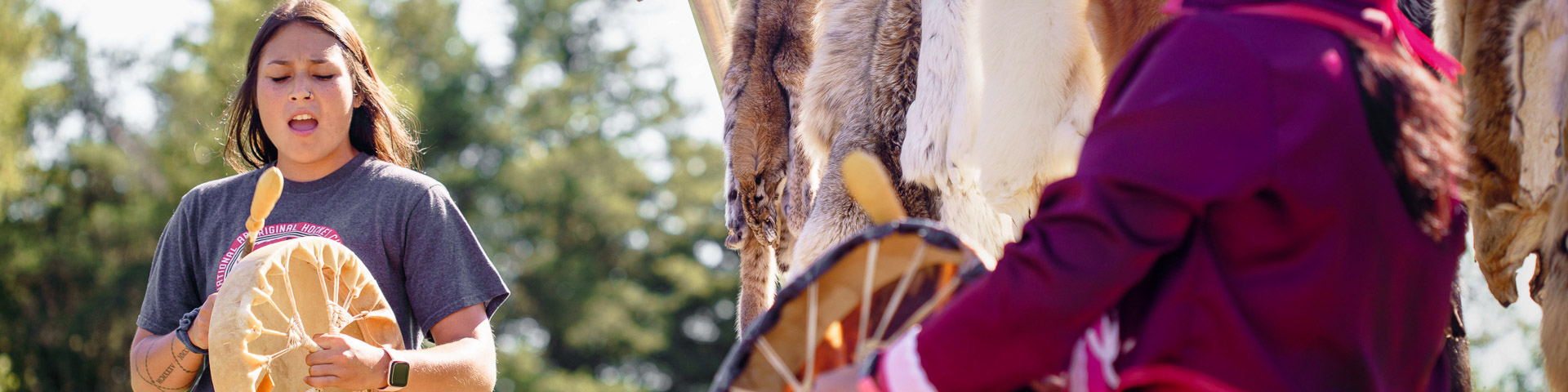 An Indigenous woman playing the drum.