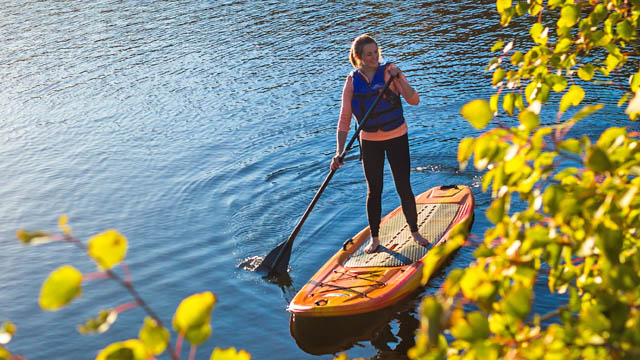 A visitor on a paddleboard on a river in the fall.