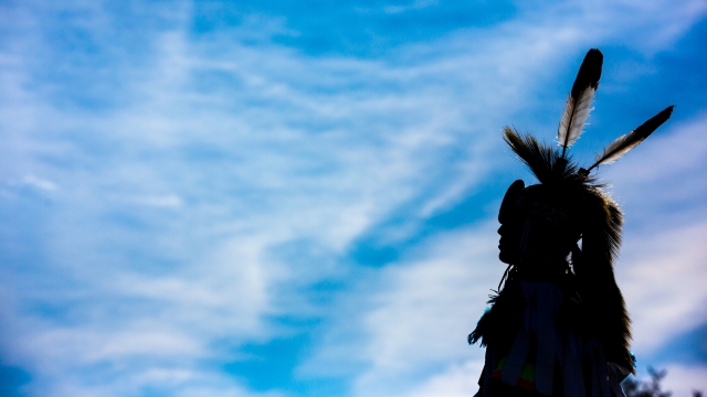 Silhouette d’une personne mi’kmaq en tenue traditionnelle, sur fond de ciel bleu.