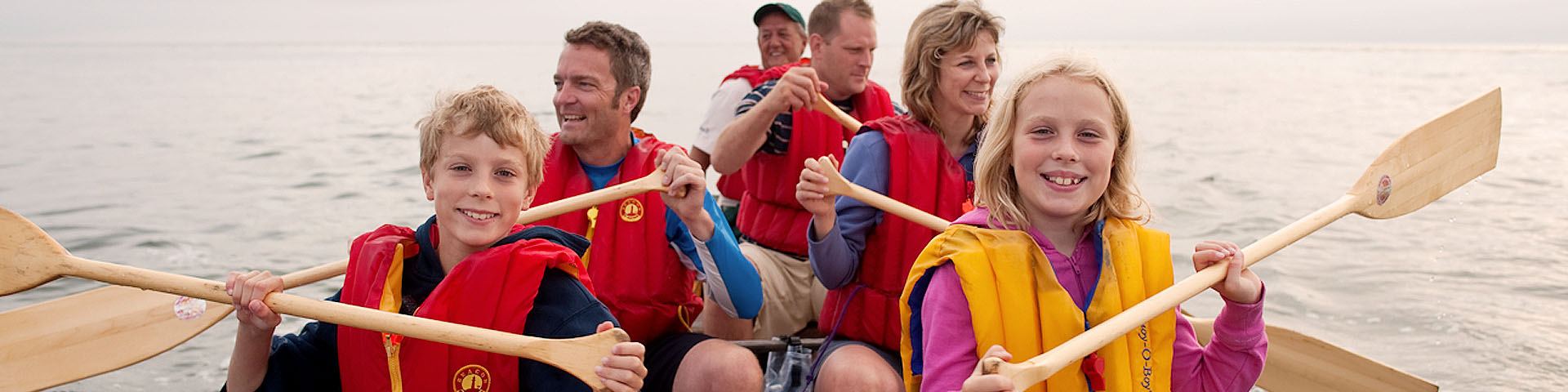 A group of people in a large canoe wearing safety vests and holding paddles.