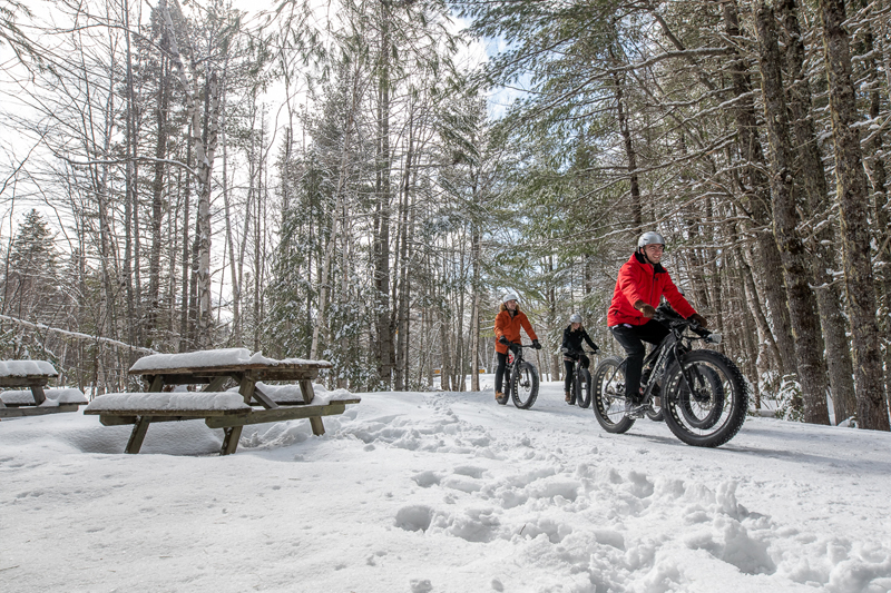 A group of visitors biking on a snow covered trail in the winter, using a fat bike