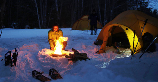 Une dame se réchauffe devant un feu de camp dans la neige