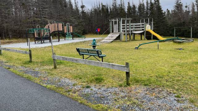 A grassy playground with climbing structures, sea-saw and park a bench