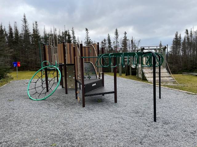 A playground with a metal climbing structure on a gravel surface