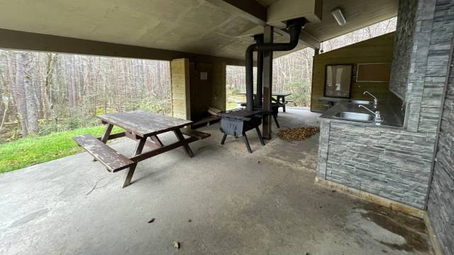 Covered concrete patio with a picnic table, wood stove, and kitchen sink