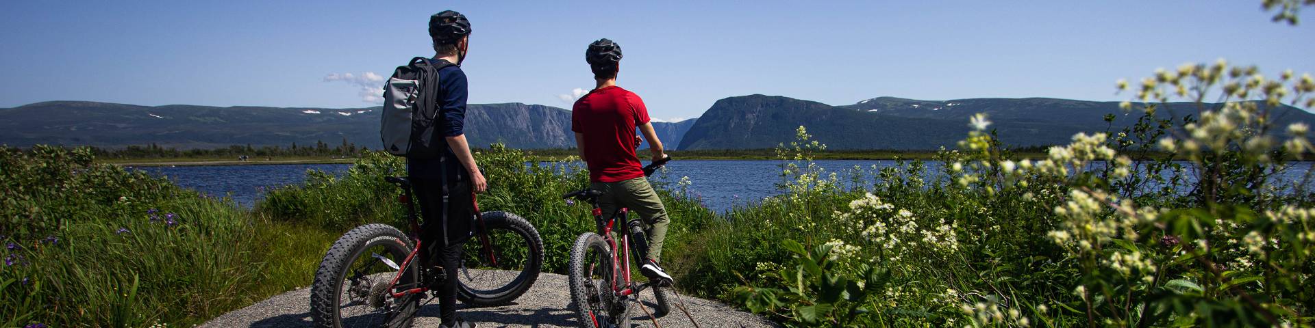 Two cyclists observing a lake with cliffs in the background.