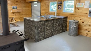 Interior of kitchen shelter with picnic tables and wood stove.