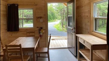 Interior of a small wooden cabin with a table and chairs and an open door.