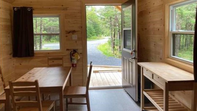 Interior of a small wooden cabin with a table and chairs and an open door.
