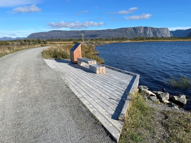 A wide path with a bench next to a pond.