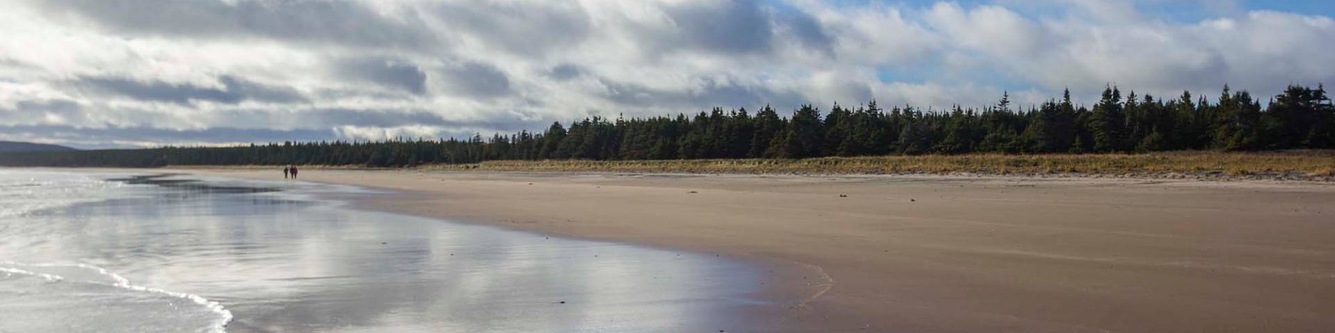 Two people walk in the distance along the beach of the Wunderstrand at Akami-Uapishkᵁ-KakKasuak-Mealy Mountains National Park Reserve