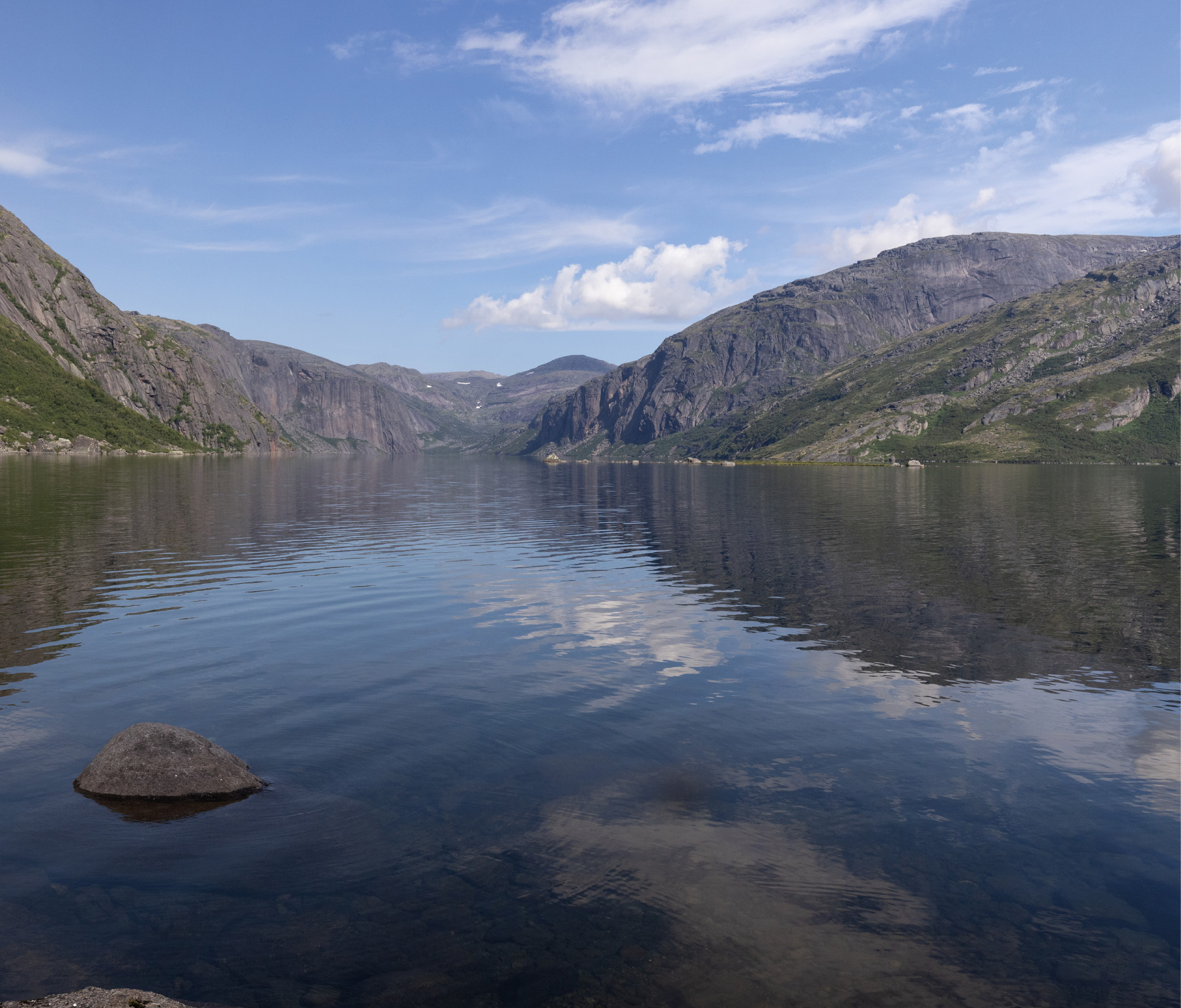 Eaux calmes avec montagnes et ciel bleu en arrière-plan.