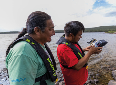 Deux hommes portant des dispositifs de flottaison vérifient l'équipement de surveillance. De l'eau en arrière-plan.