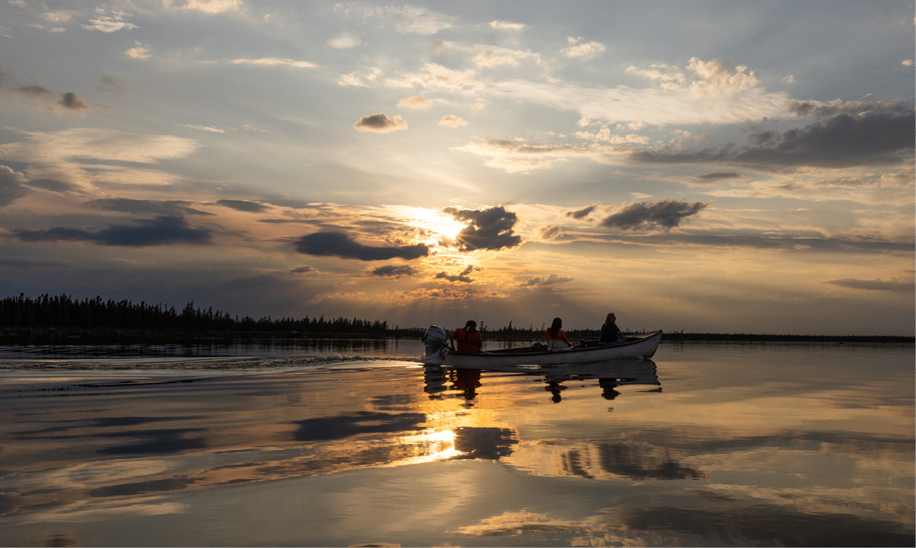 Trois personnes dans un bateau sur des eaux calmes au coucher du soleil.