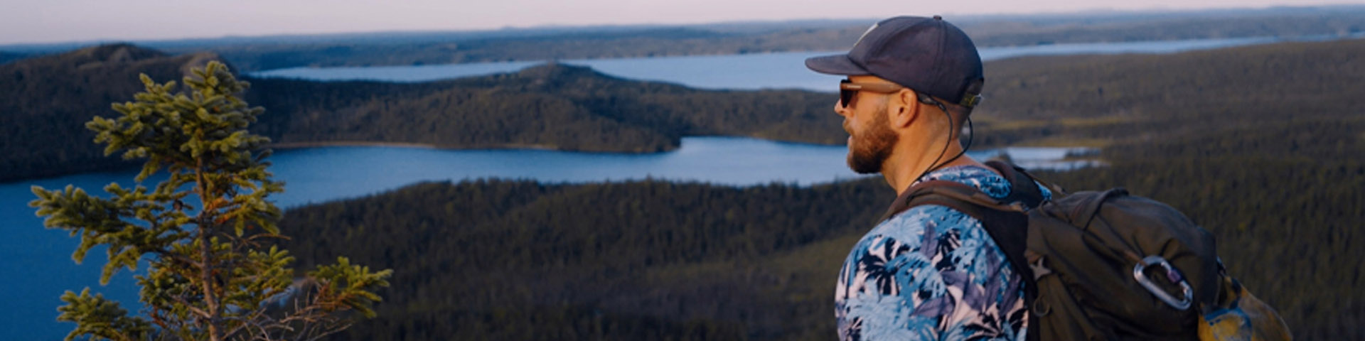 an individual wearing a backpack and a baseball cap looks out over a coastal view