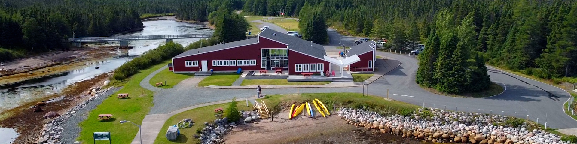 a red building on the coast with colourful kayaks on the beach