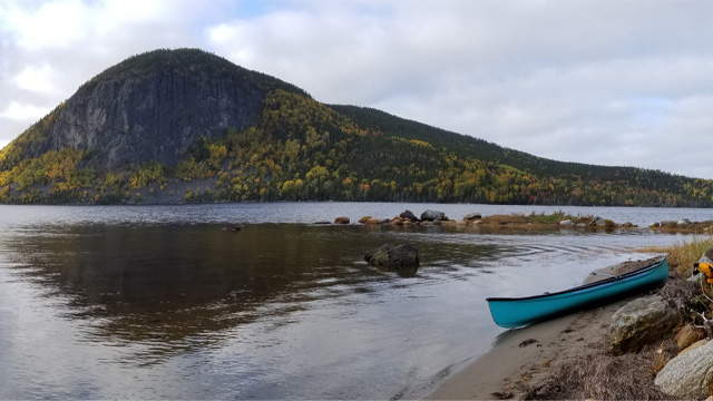 Un canoë bleu clair sur une plage près d'un plan d'eau calme à flanc de colline.
