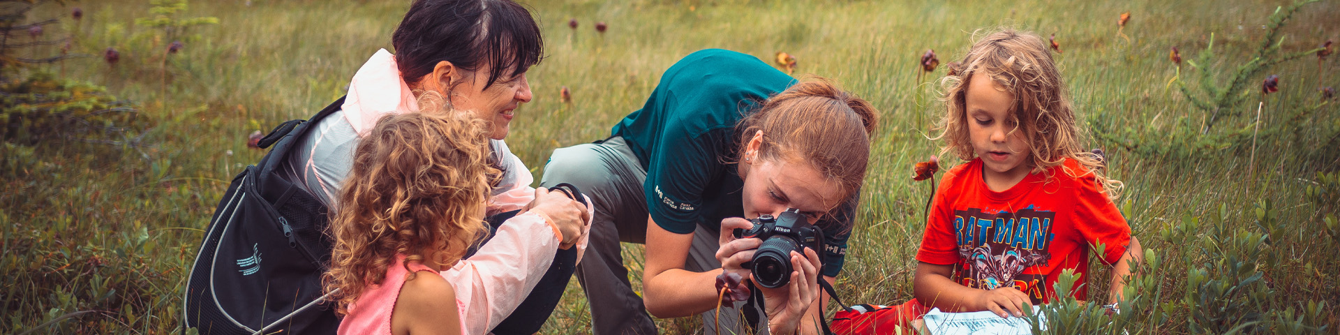 a Parks Canada employee taking a photo of something on the ground, with a small group of adults and children