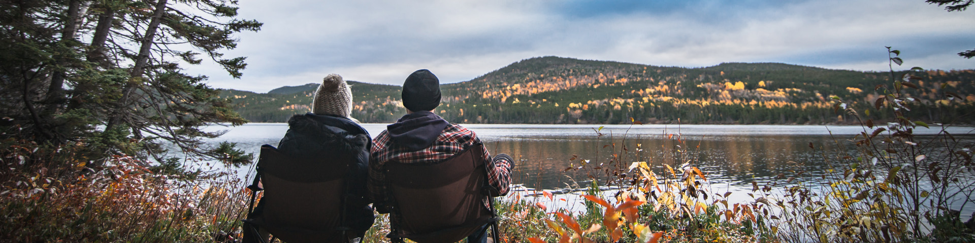 deux individus portant des bonnets de laine, assis dans des chaises de camping, surplombant une scène d'automne