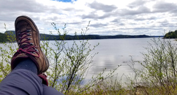 a person's hiking boots overlooking a pond