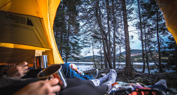 two people with a mug looking out of a yellow tent at a water-side view