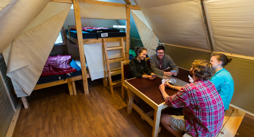 four people sitting around a table inside an oTENTik playing cards