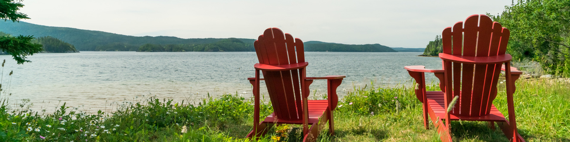 two red Adirondack chairs overlooking an ocean inlet