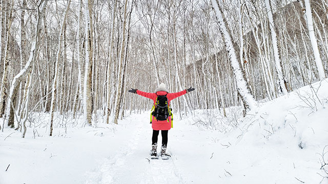 Une personne, dos à la caméra, marchant en raquette dans une forêt enneigée, les bras grands ouverts.