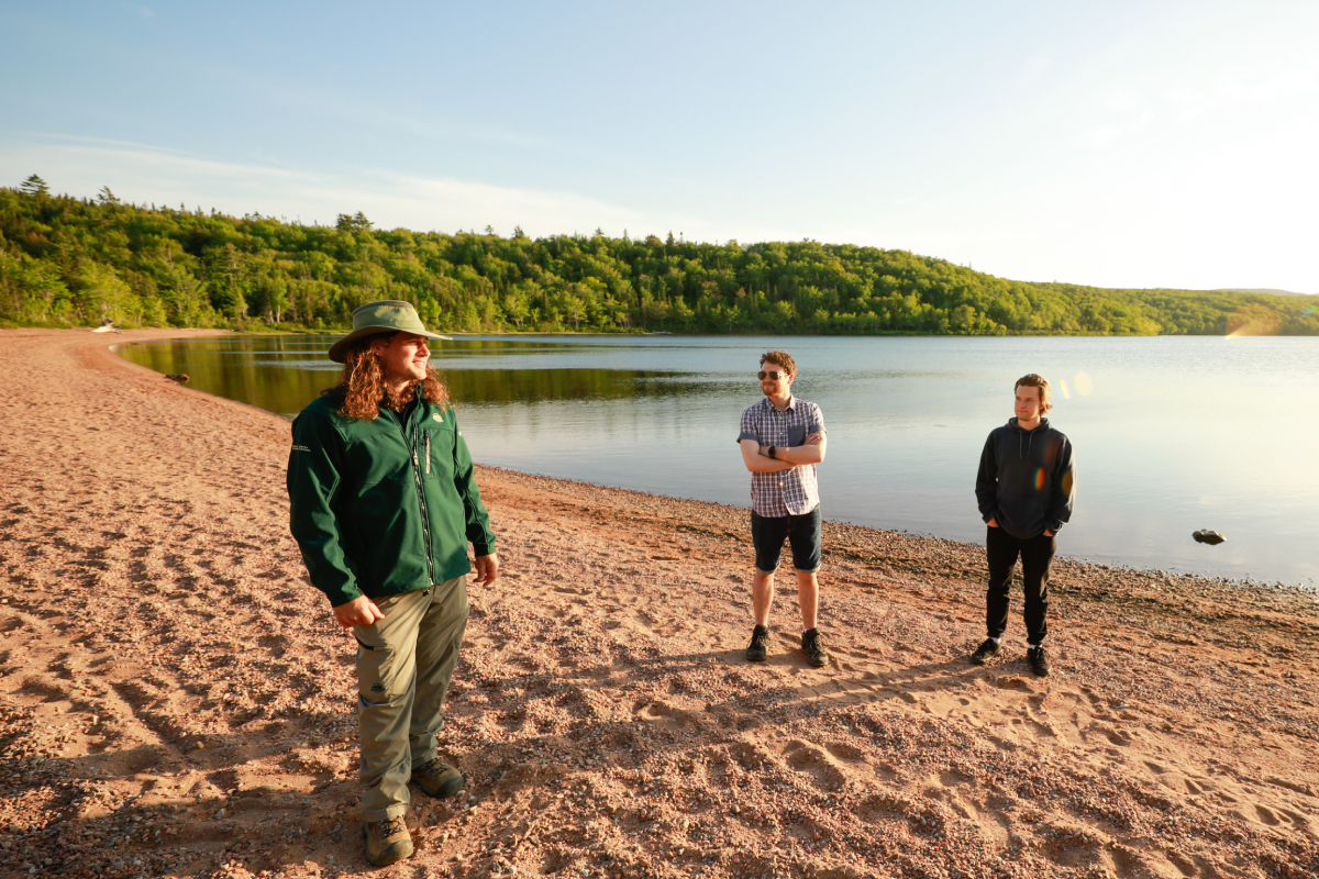 Un guide discute avec deux visiteurs sur une plage de sable au coucher du soleil.