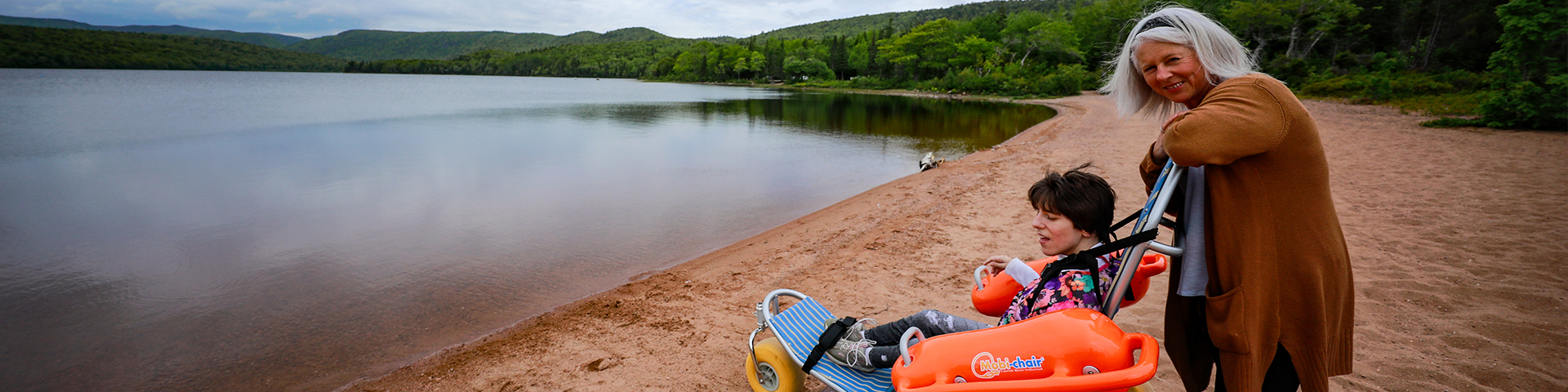 A person pushes a beach wheelchair toward the water with another person seated in it.