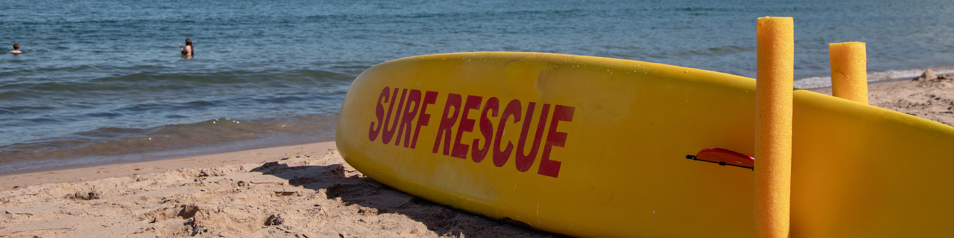 A yellow rescue surfboard lies on a sandy beach.